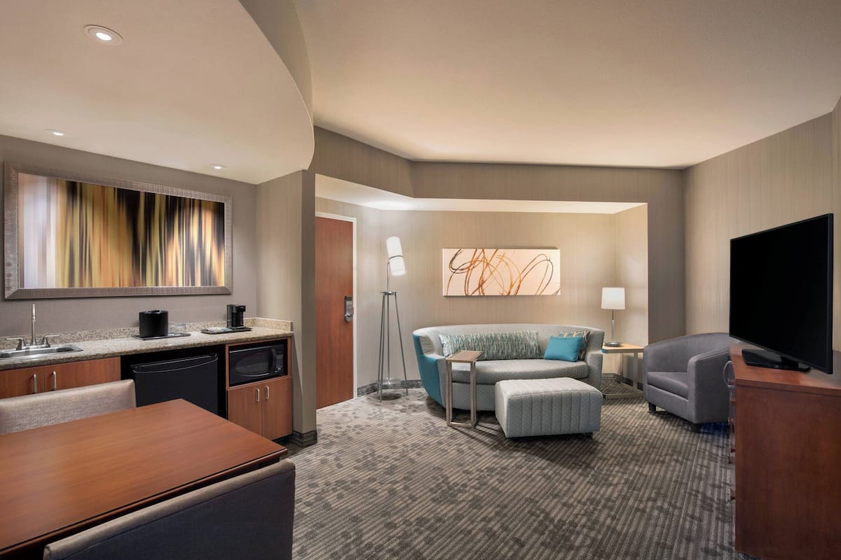A hotel room with a kitchenette, a sofa, a TV, and a large abstract painting on the wall.