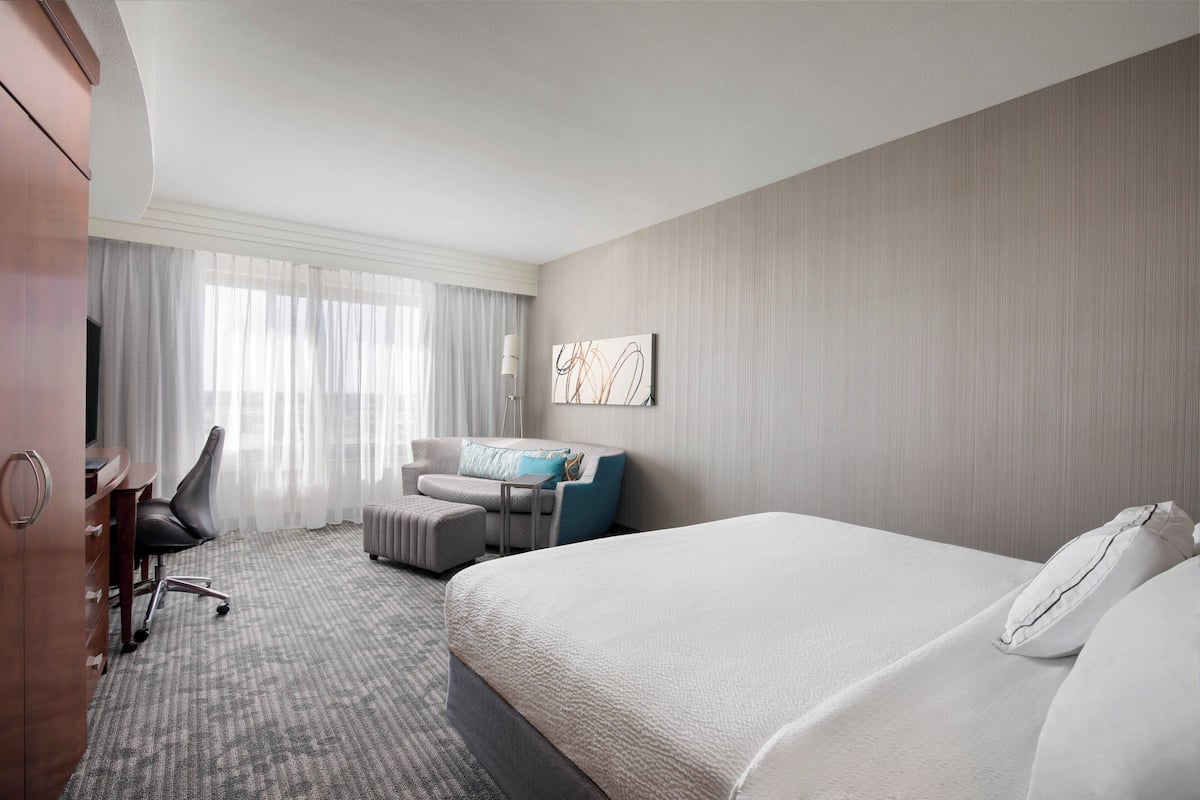 A hotel room with a large bed, a desk with a chair, a small table, and a sofa.