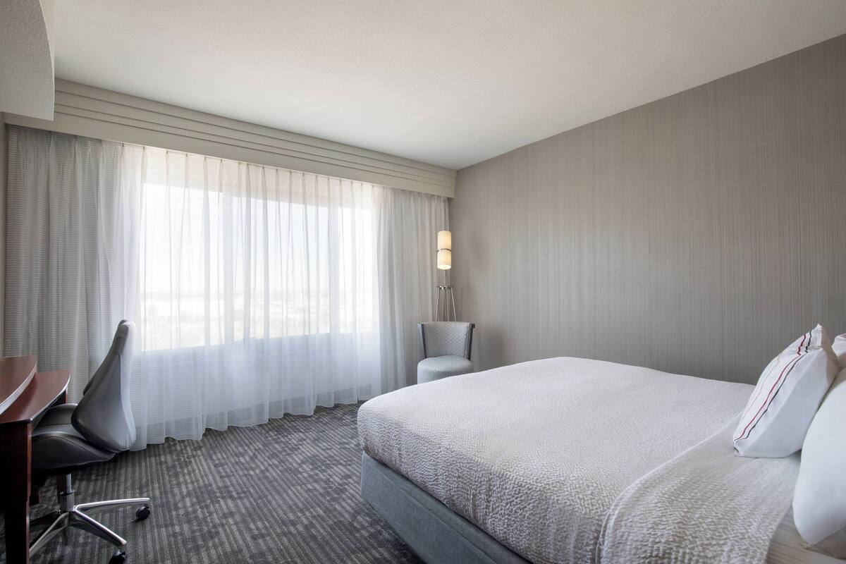 A hotel room with a large bed, a desk, a chair, and a lamp.