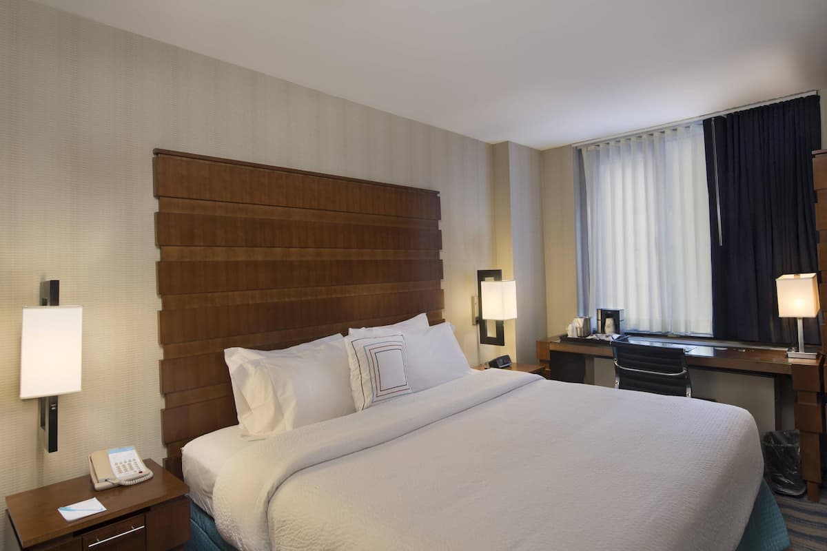 Habitación de hotel con una cama grande, un escritorio, una silla, un teléfono y una ventana con cortinas.