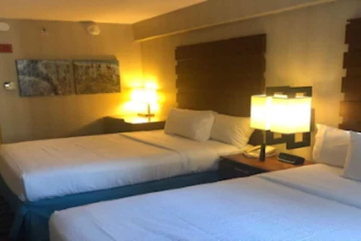 Una habitación de hotel con dos camas, una mesita de noche con lámpara y un cuadro en la pared.