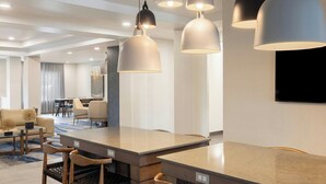 Een moderne hotellobby met een bar in het midden, zitgedeeltes en hanglampen.