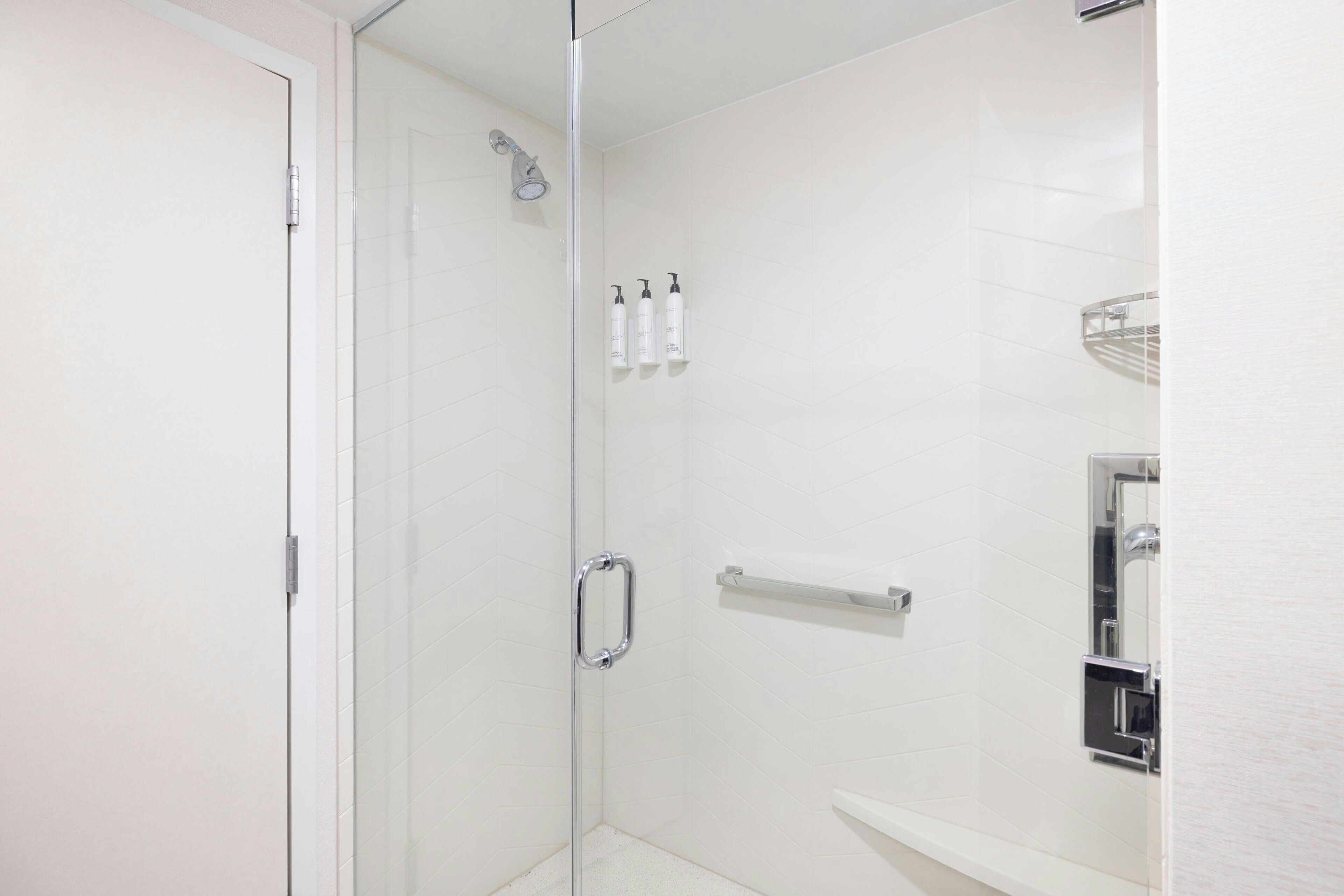 Ein modernes Badezimmer mit einer gläsernen Duschkabine, einer weißen Fliesenwand und einem chromfarbenen Handtuchhalter.