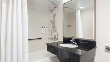 Un bagno moderno con lavabo su piano nero, vasca da bagno bianca e doccia con soffione manuale.