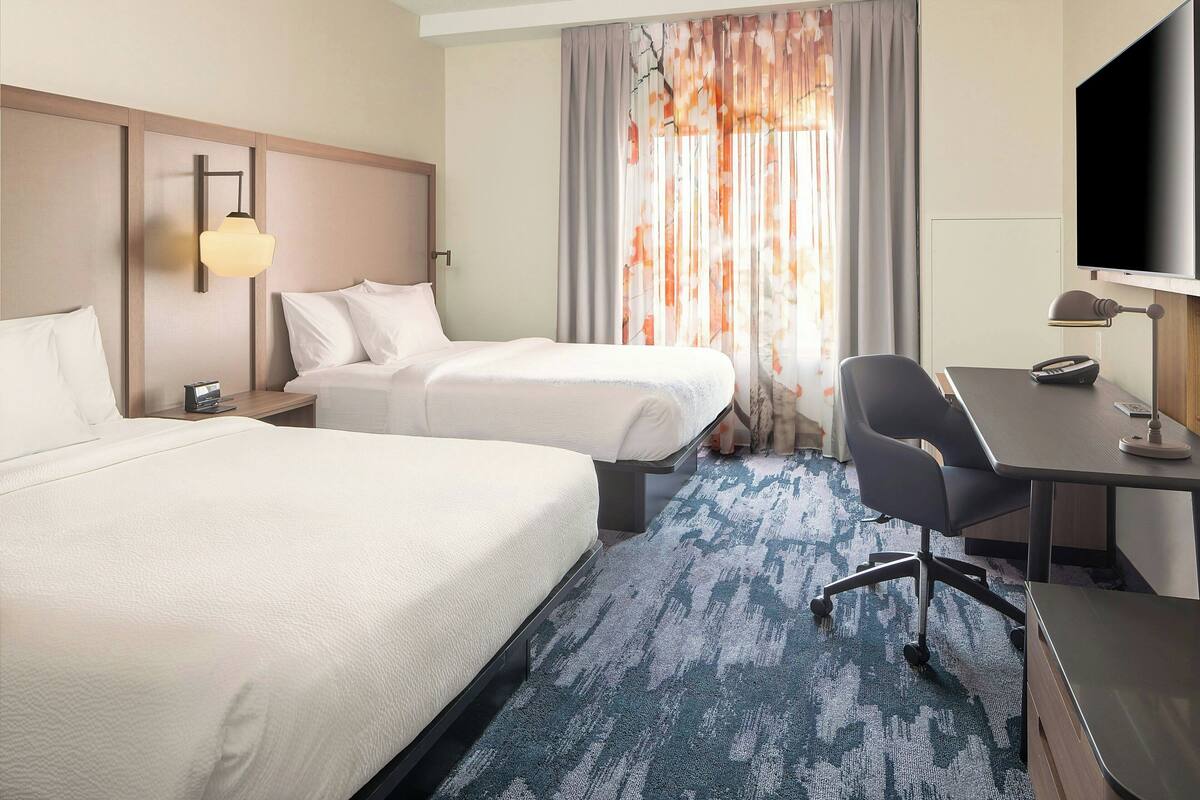 Habitación de hotel con dos camas, un escritorio, una silla, un televisor y una lámpara.