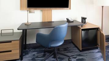 A modern office desk with a blue chair, a flat-screen TV, a lamp, a phone, and a coffee machine.