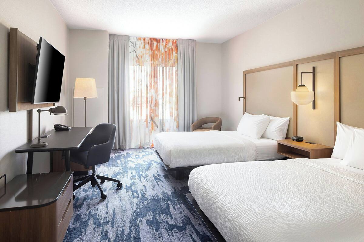 Habitación de hotel con dos camas, un escritorio, una silla, un televisor y una lámpara.