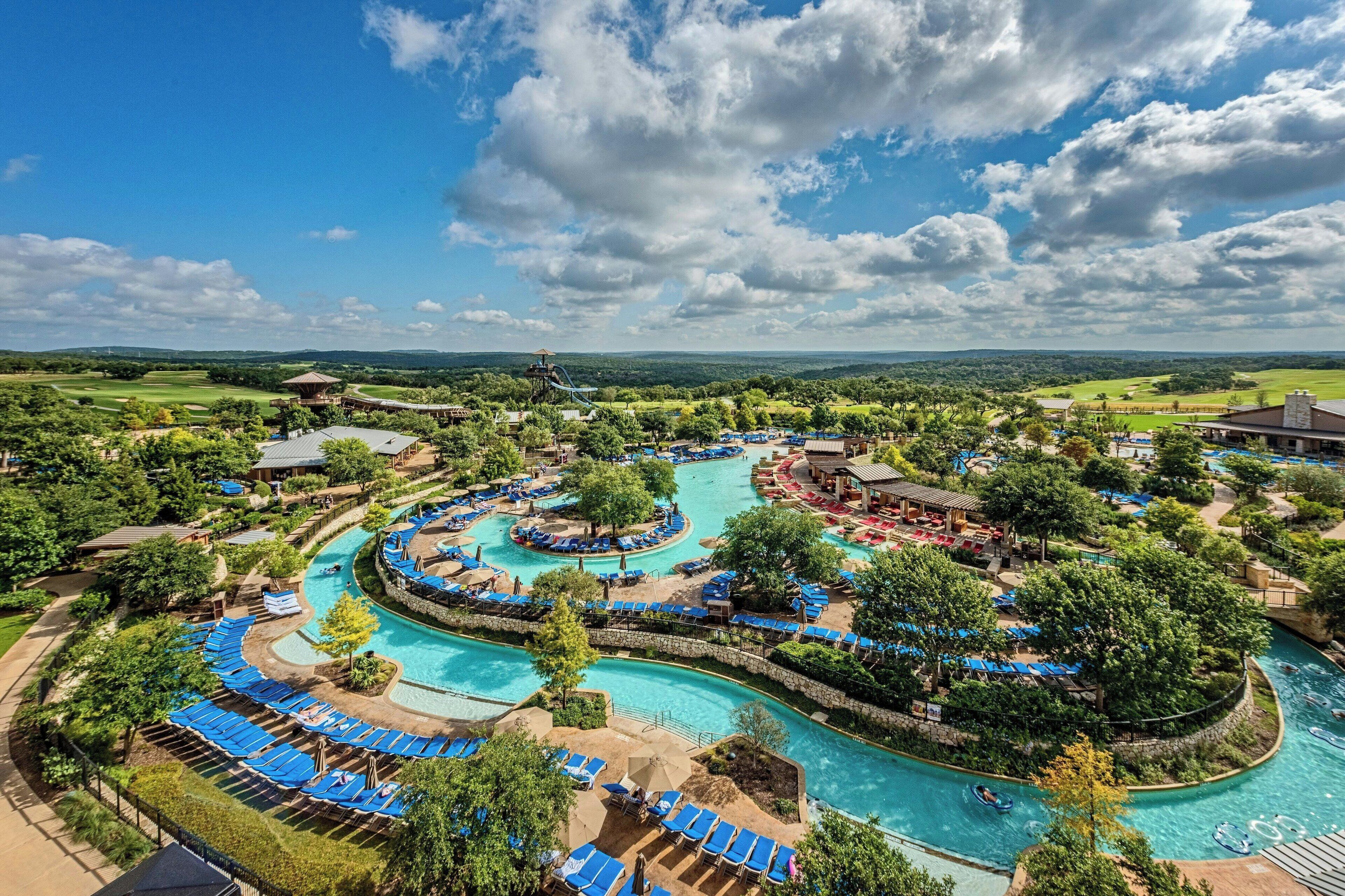 Un resort con un amplio área de piscina, varias toboganes acuáticos y una vista panorámica del paisaje circundante.