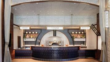 A pizza restaurant interior with a central pizza oven, order and pick-up counters, and a decorative ceiling.
