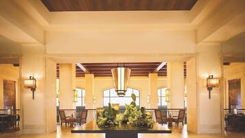 A spacious lobby with a central table adorned with flowers, high ceilings with wooden beams, and large windows providing natural light.