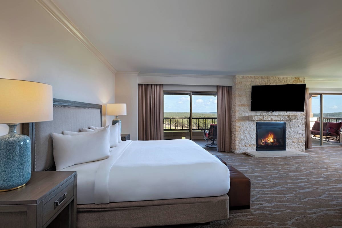 Una habitación de hotel con una cama grande, un televisor de pantalla plana en la pared, una chimenea y un balcón con mobiliario exterior.