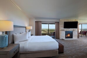 Una habitación de hotel con una cama grande, un televisor de pantalla plana en la pared, una chimenea y un balcón con mobiliario exterior.