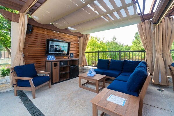An outdoor patio with wooden furniture, a TV, and a pergola.
