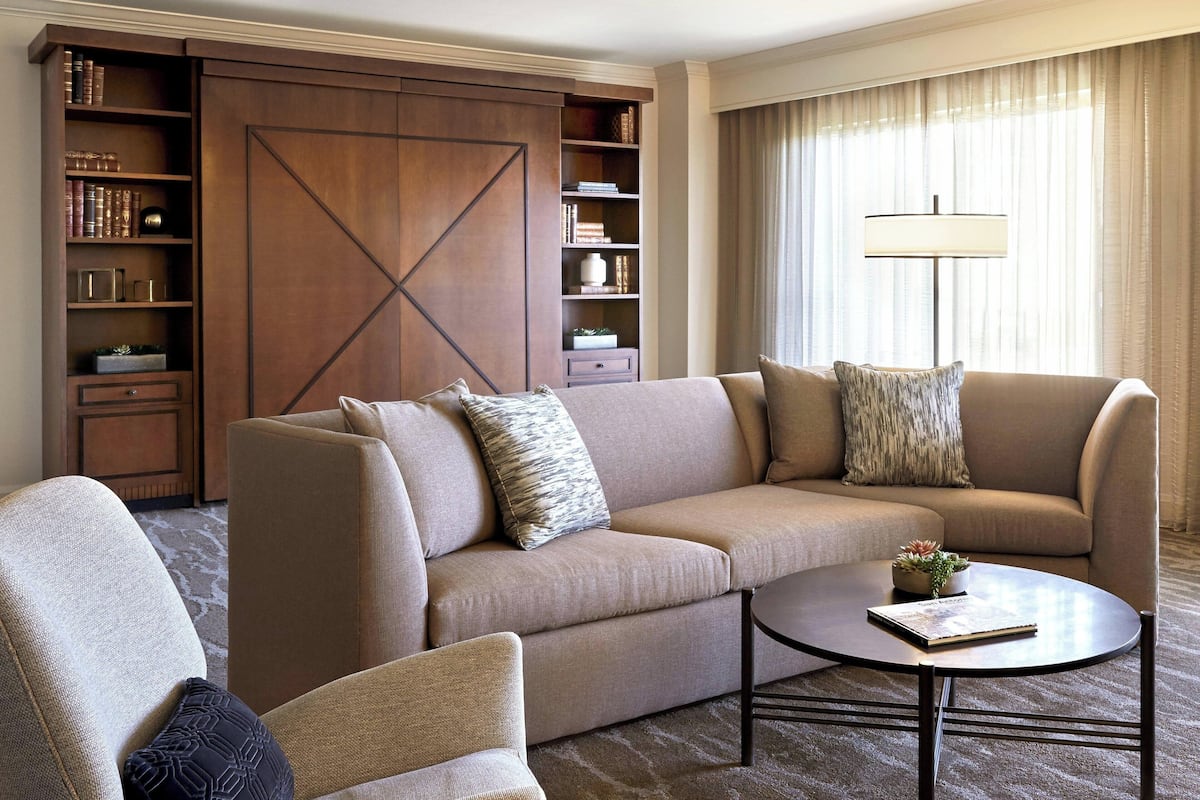 Una sala de estar moderna con un sofá, un sillón y una mesa de centro. Se observa una estantería con libros y objetos decorativos.