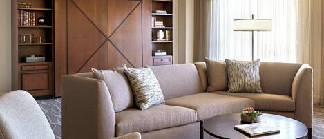 A modern living room with a sofa, armchair, and a coffee table. There is a bookshelf with books and decorative items.