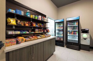 Zona de aperitivos y bebidas autoservicio, con bebidas refrigeradas y un cajero automático.