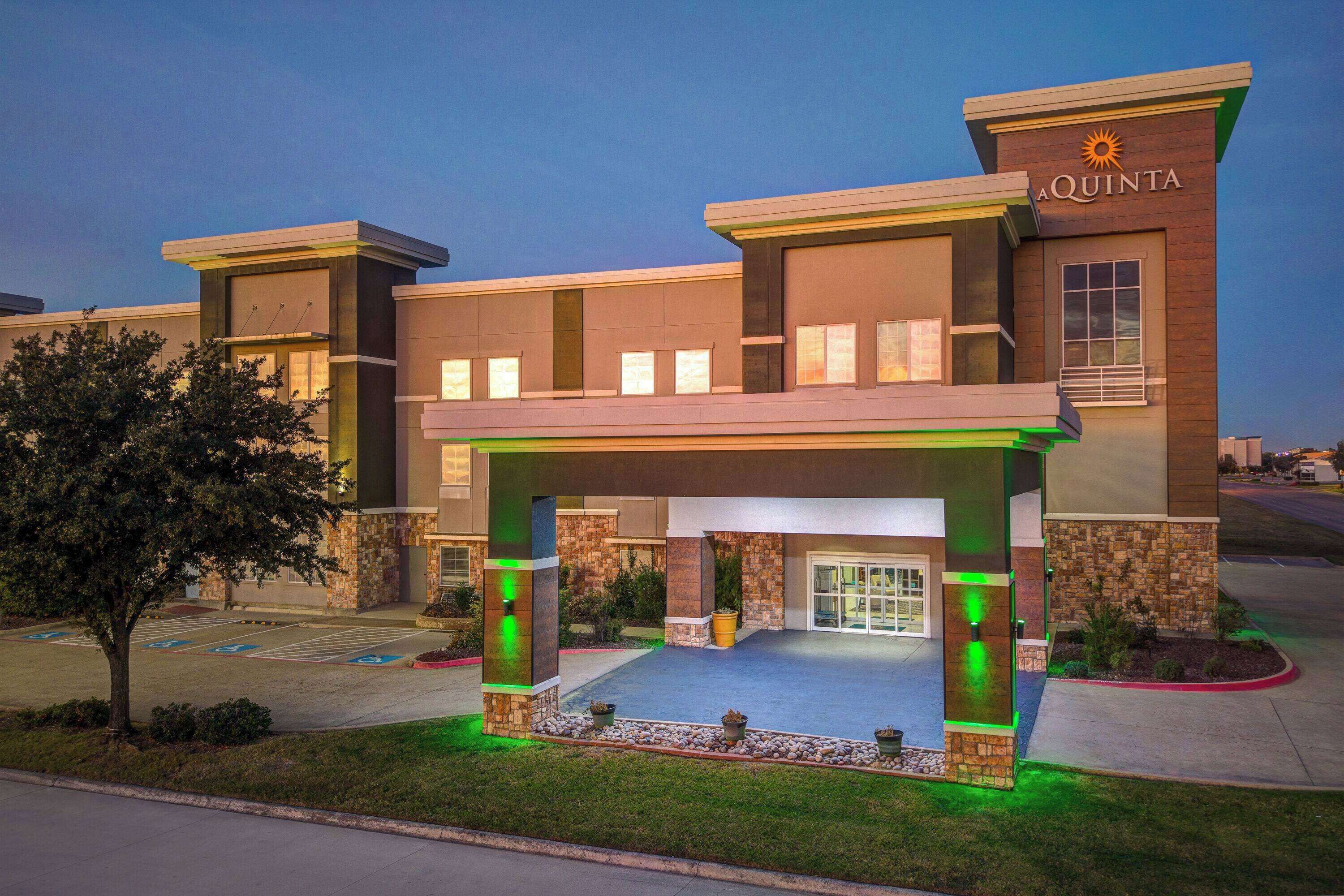 A hotel entrance with a covered driveway, a parking lot, and a sign reading "AQUINTA".