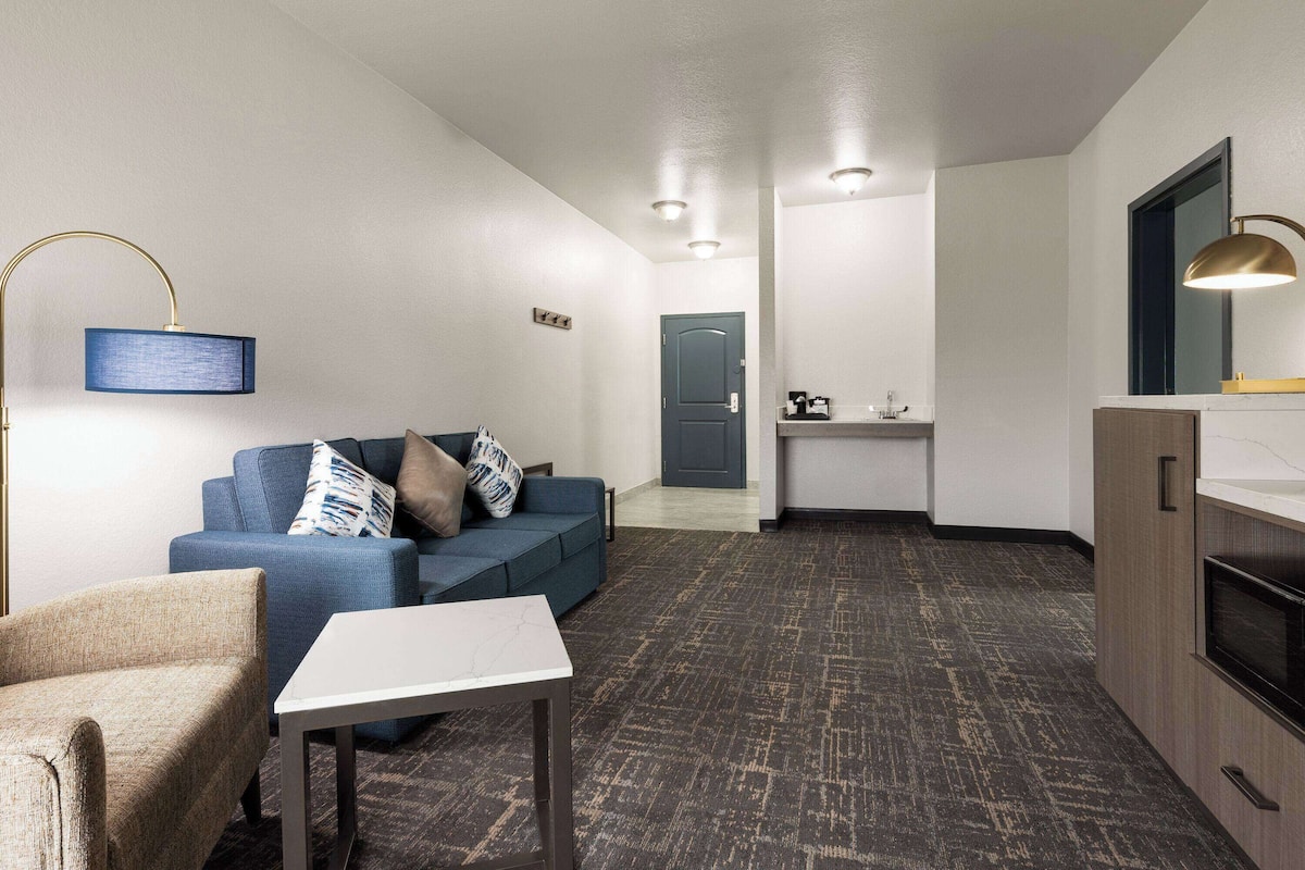 A modern living room with a sofa, a coffee table, and a lamp. There is a kitchen area with a microwave and a sink.
