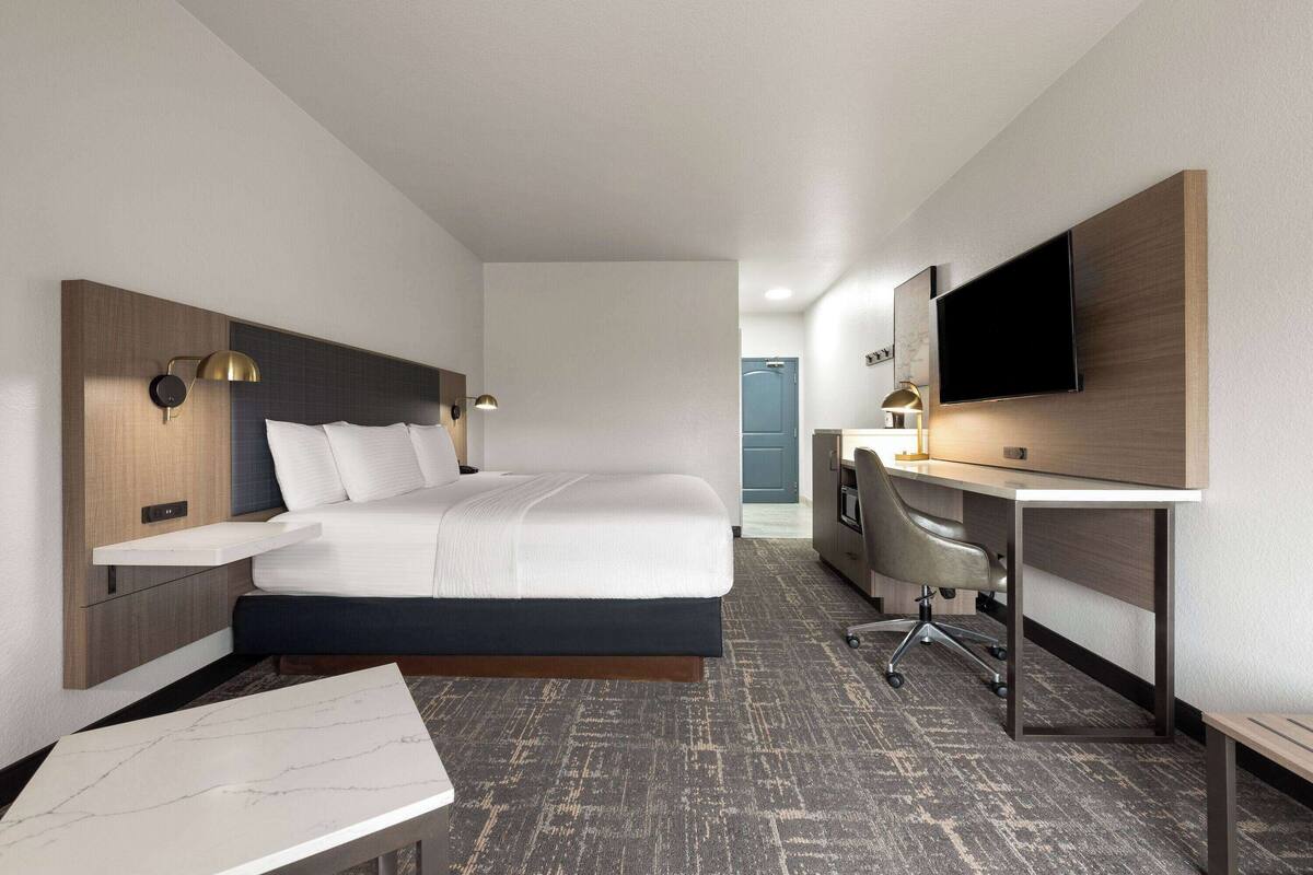 A hotel room with a bed, desk, chair, and TV.