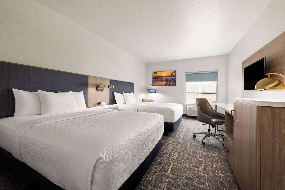 A hotel room with two beds, a desk, a chair, a TV, and a window with a view of a bridge.