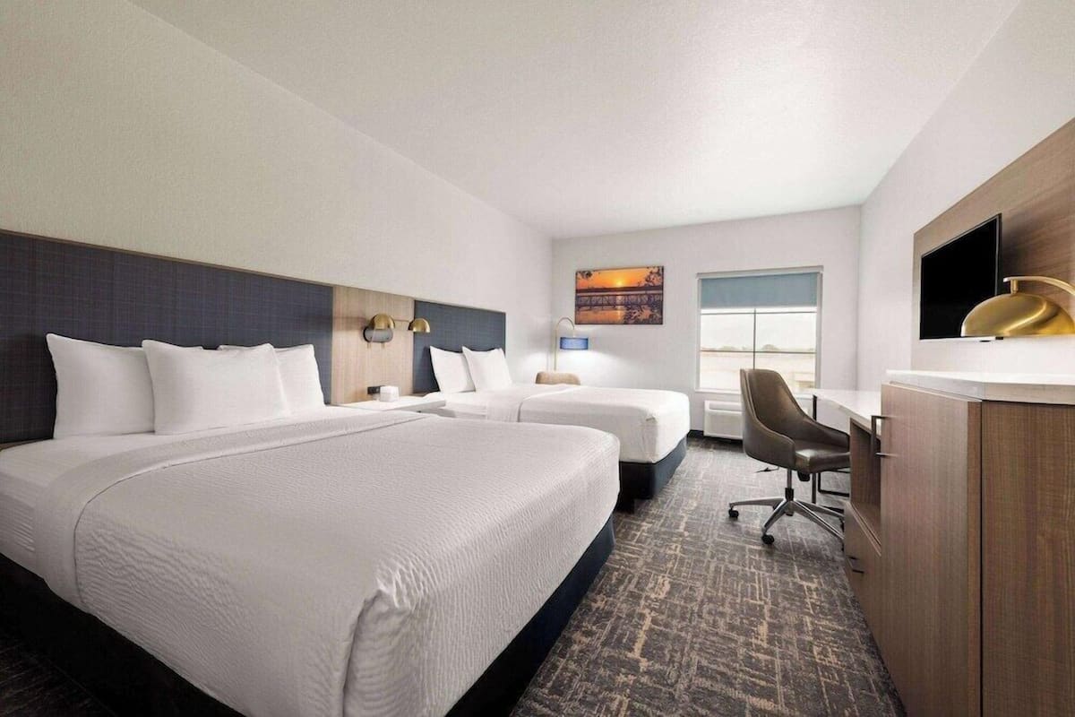 A hotel room with two beds, a desk, a chair, a TV, and a window.