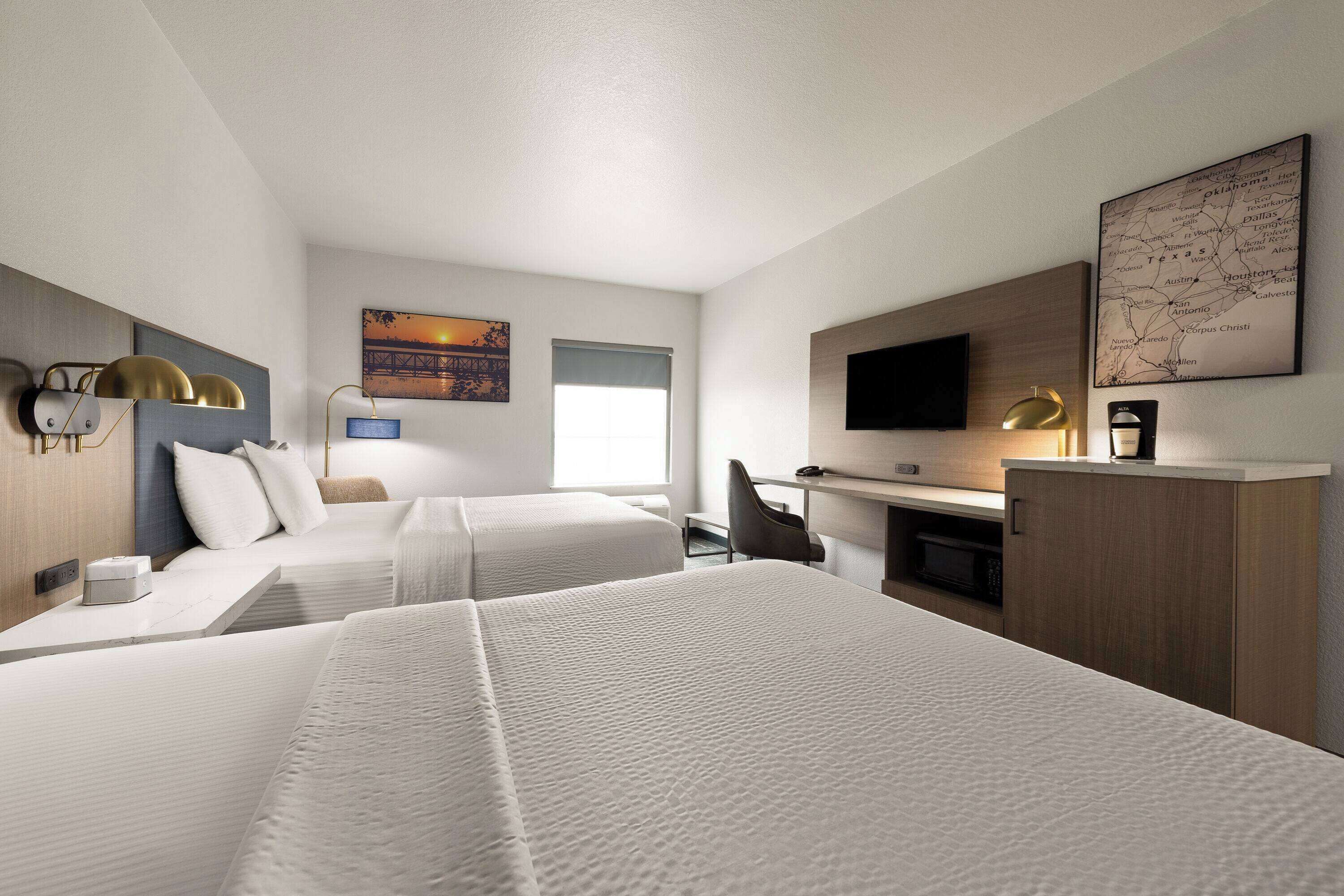 Quarto de hotel com duas camas, uma escrivaninha, uma cadeira, uma televisão e um mapa na parede.