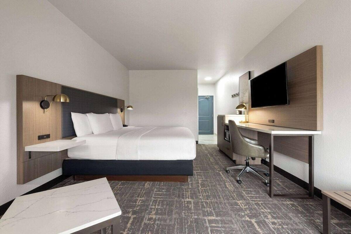 A hotel room with a bed, desk, chair, TV, and a small table.