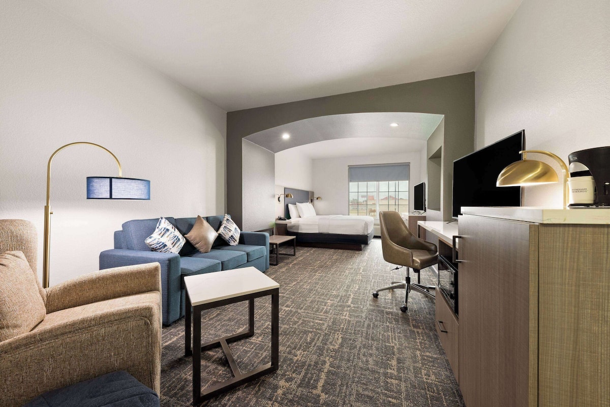 A hotel room with a bed, a blue sofa, a desk with a chair, a small table, and a lamp.