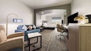 Habitación de hotel con cama, sofá azul, escritorio con silla, mesita pequeña y lámpara.