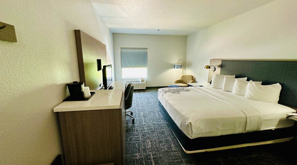 A hotel room with a bed, desk, chair, and a large window.