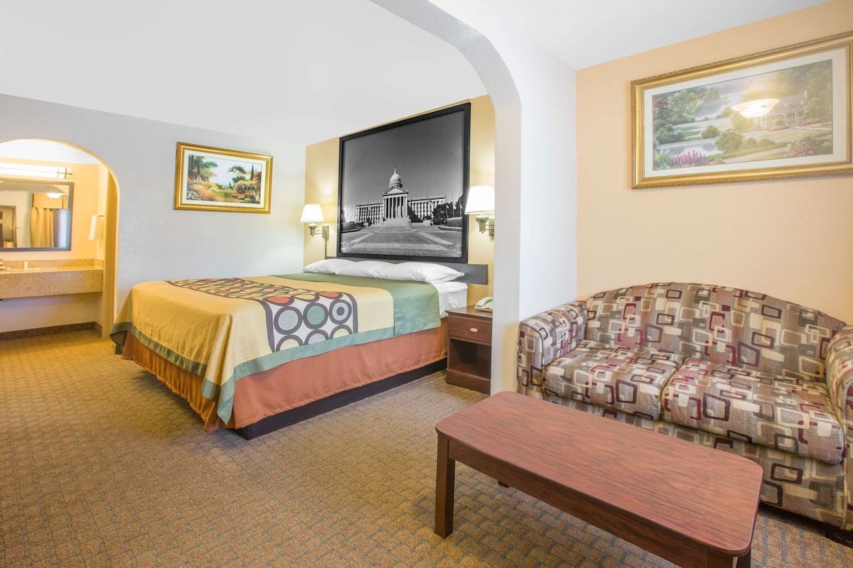 A hotel room with a bed, a sofa, a small table, a mirror, and two framed pictures on the walls.
