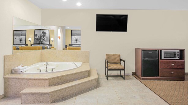A modern bathroom with a freestanding bathtub, a chair, a microwave, and a refrigerator. - Super 8 by Wyndham Idabel (Idabel)