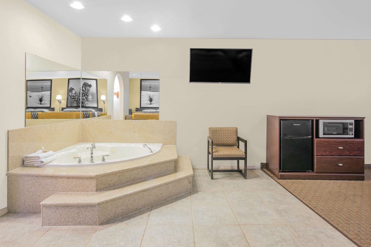A modern bathroom with a freestanding bathtub, a chair, a microwave, and a refrigerator.