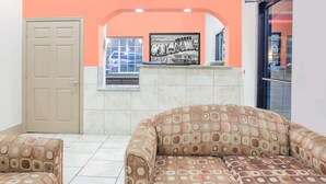 A room with a beige door, a patterned sofa, and a tiled floor. - Super 8 by Wyndham Idabel (Idabel)