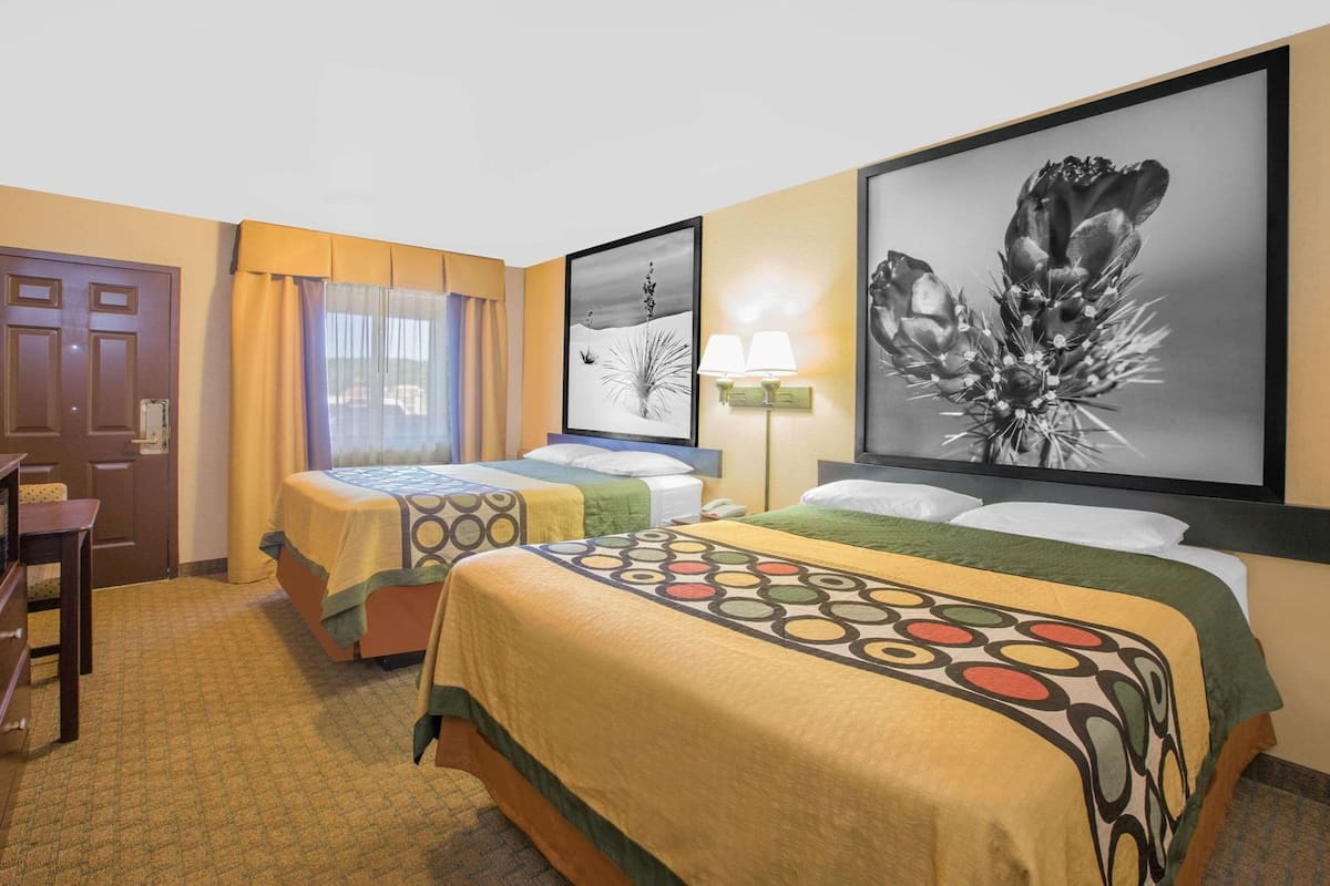 A hotel room with two beds, a desk, a chair, and artwork on the walls.