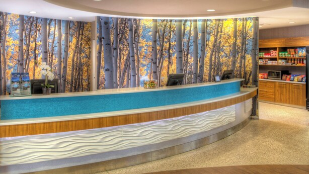 A reception area with a curved counter, a wall mural of trees, and a snack bar with packaged goods. - SpringHill Suites Anchorage University Lake (Anchorage)