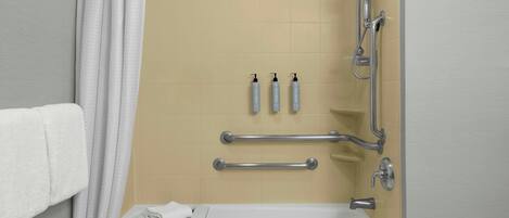 A bathroom with a bathtub, grab bars, a towel rack, and three bottles of lotion on the wall.