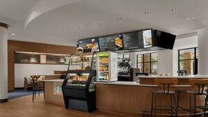 A modern Starbucks with a self-serve coffee machine, a menu display, and a seating area with wooden chairs and a counter.