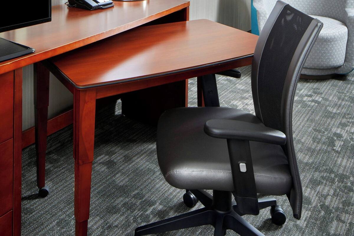 Une chambre d’hôtel avec un bureau en bois, un fauteuil de bureau noir, un téléphone et une lampe.