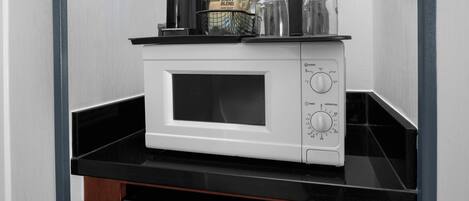 A microwave oven on a black countertop with a coffee maker, a bag of coffee, and a glass container.
