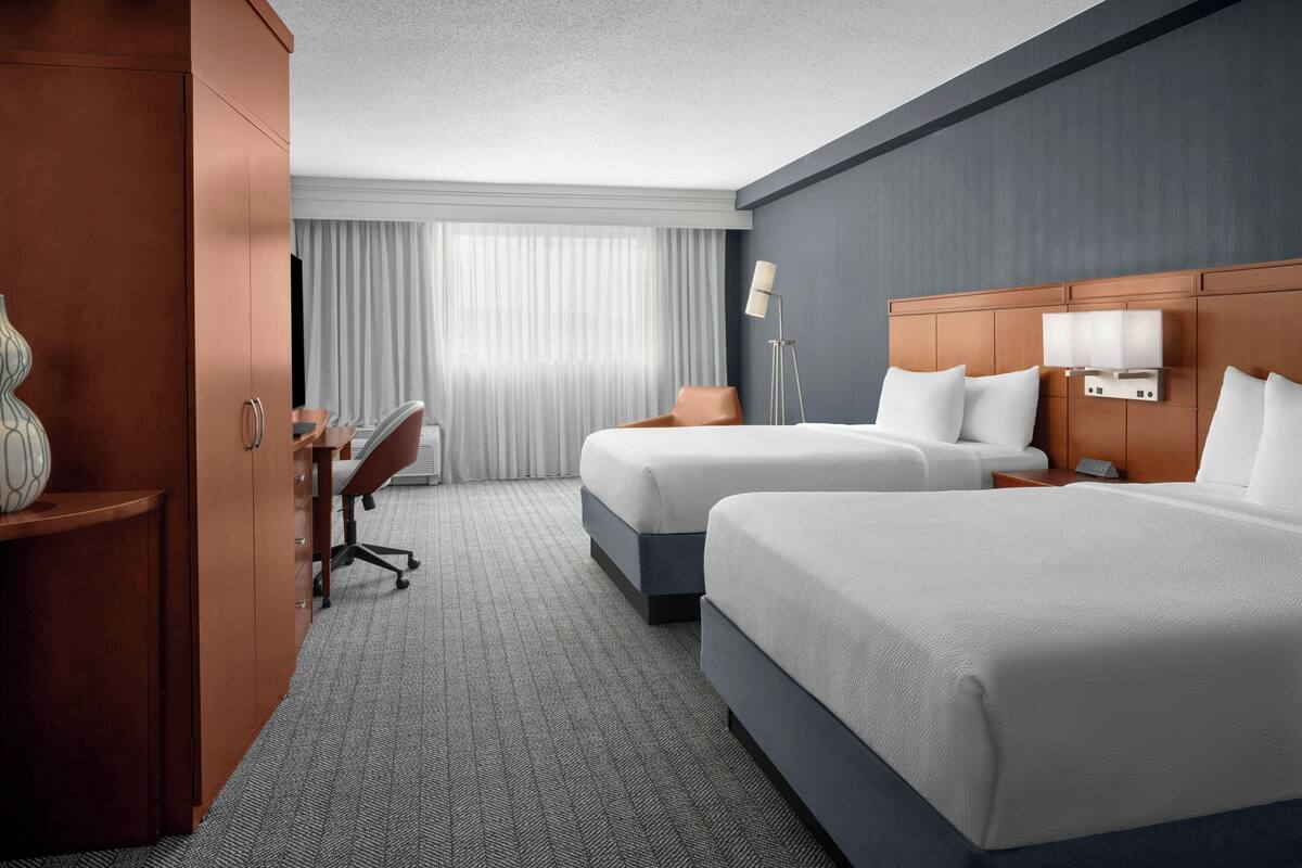 Une chambre d’hôtel avec deux lits, un bureau, une chaise, une lampe et une armoire.
