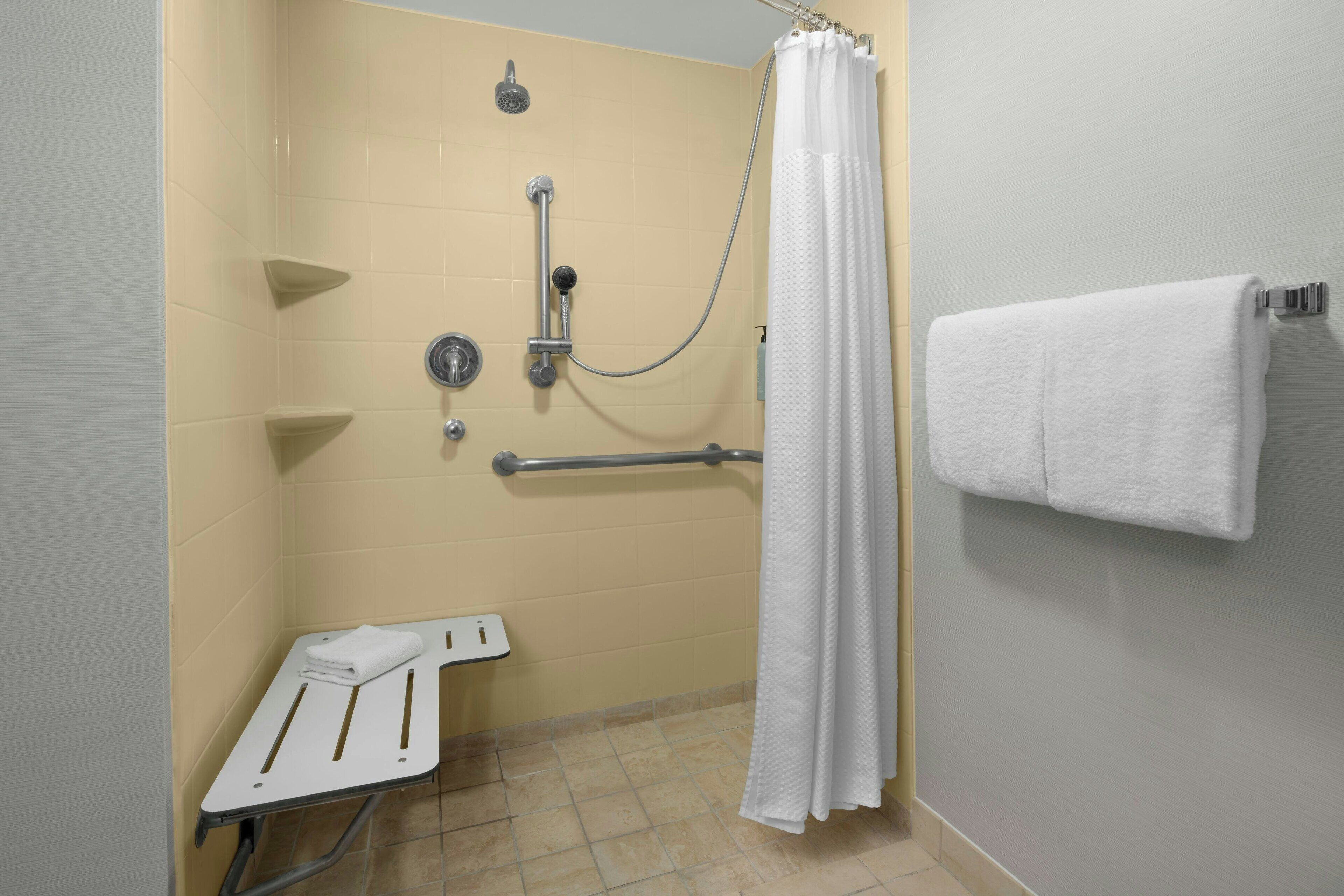 Een badkamer met een douche, handgrepen, een witte handdoekhouder en een bankje.