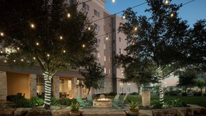An outdoor patio area with a fire pit, green Adirondack chairs, and string lights.