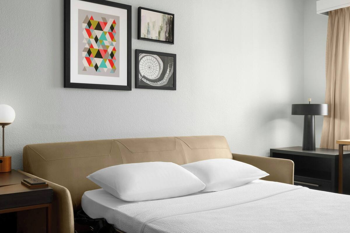 A hotel room with a bed, a nightstand, a lamp, and framed artwork on the wall.