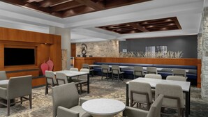Un vestíbulo de hotel con diversas zonas de estar, incluyendo un bar y una sala con un muro de acento de piedra.