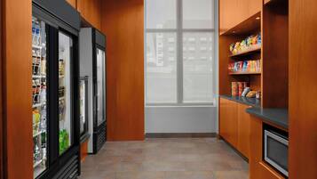 A narrow hallway with wooden walls, a refrigerator, a microwave, and shelves with snacks.