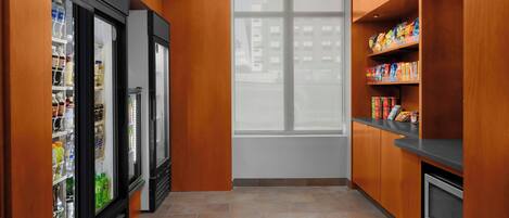 A narrow hallway with wooden walls, a refrigerator, a microwave, and shelves with snacks.
