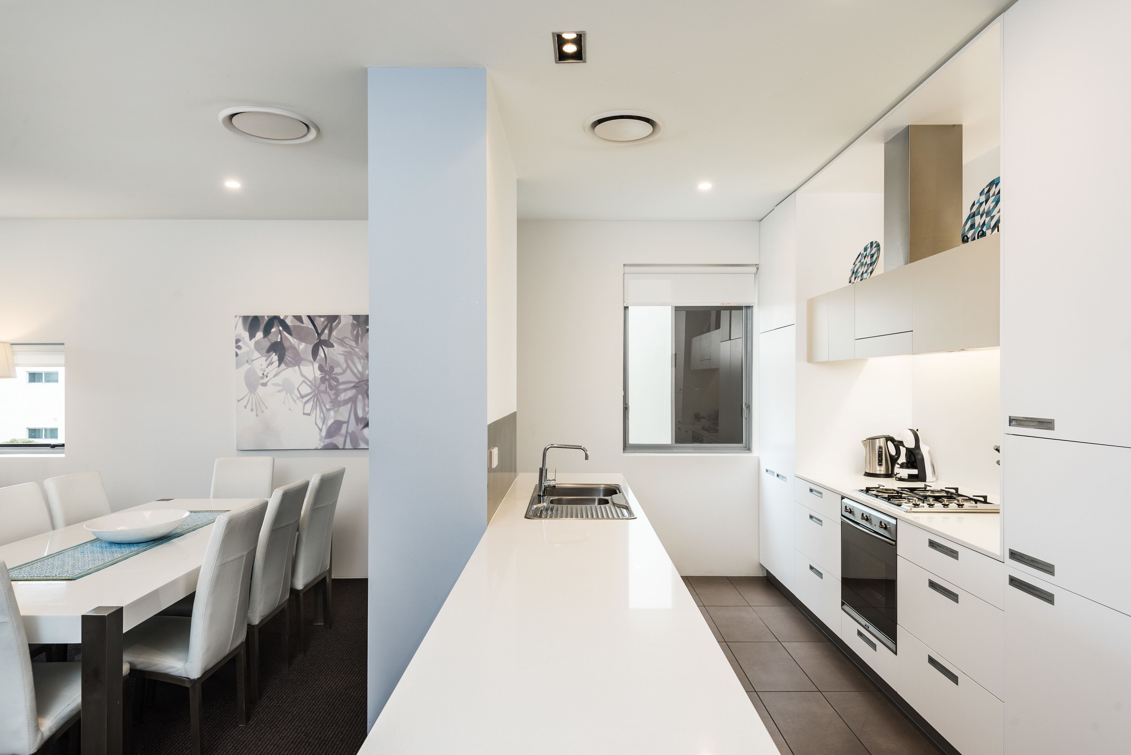 Una cocina moderna con armarios blancos, estufa integrada y un comedor con mesa y sillas blancas.