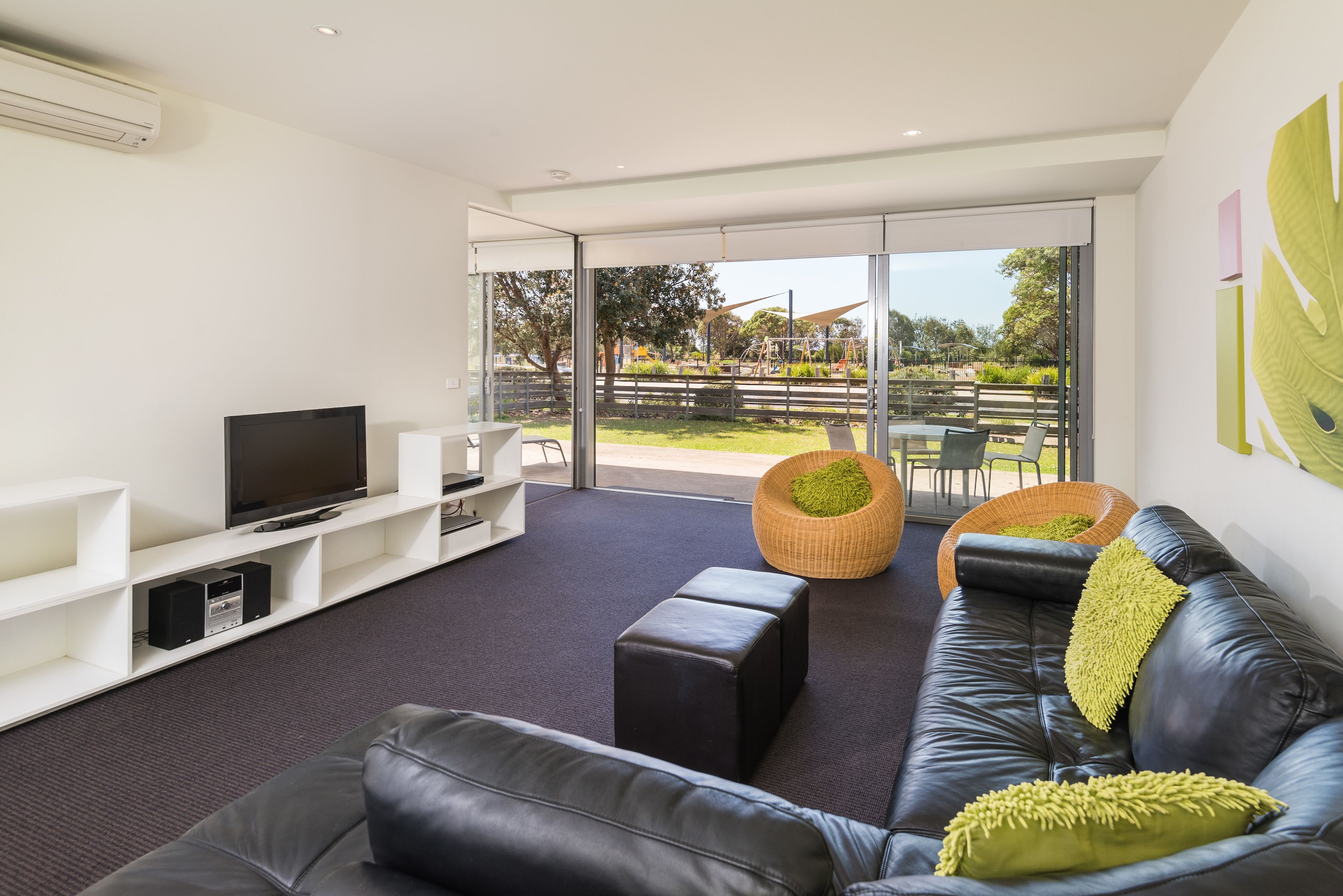 A modern living room with a leather sofa, a flat-screen TV, and a large glass door leading to an outdoor area.