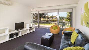 A modern living room with a leather sofa, a flat-screen TV, and a large glass door leading to an outdoor area.